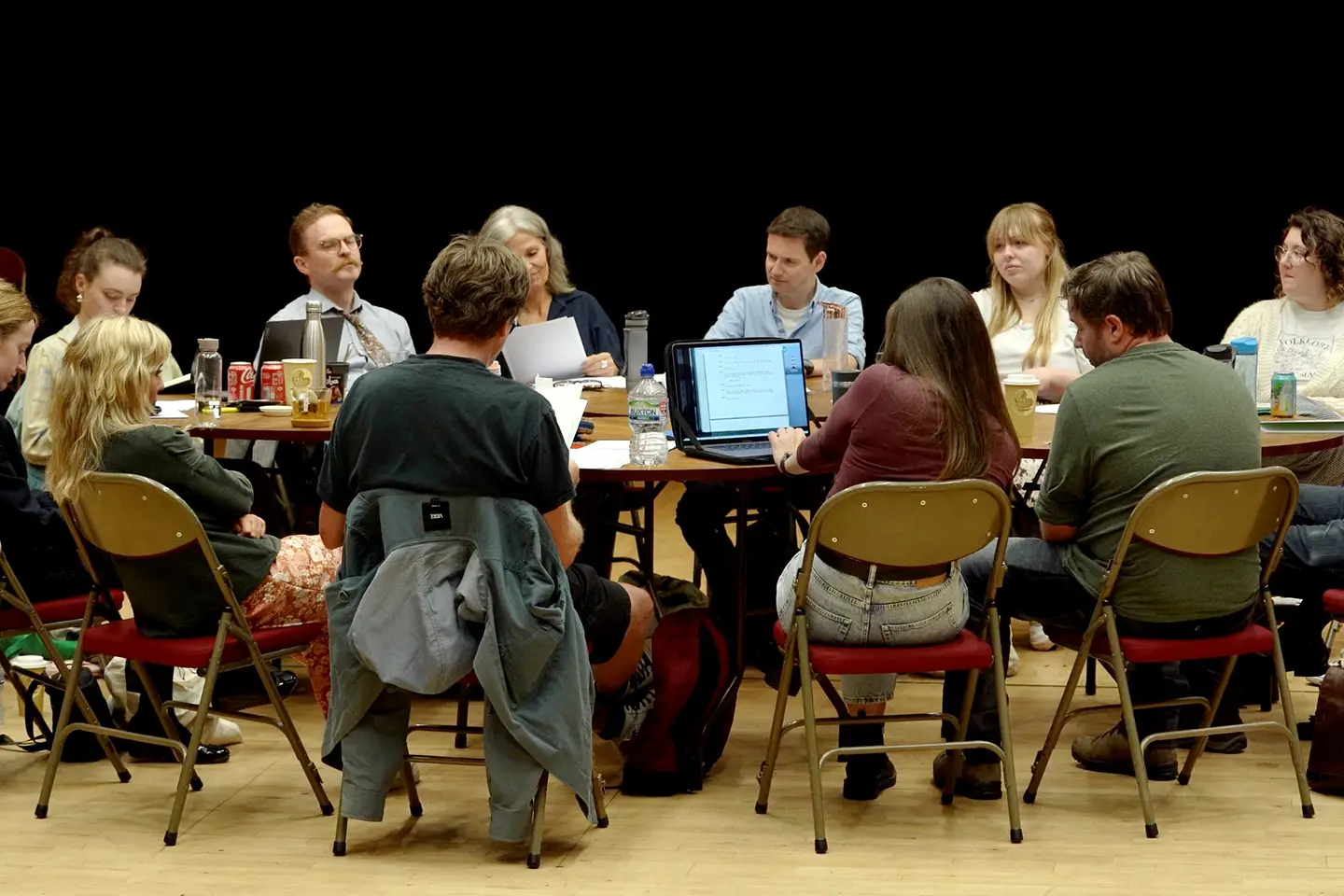 A diverse group of writers sit around a table discussing their work.